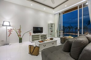 Ein modernes Wohnzimmer mit Flachbildfernseher, weißen Möbeln, einer Glasvitrine und Blick ins Freie.