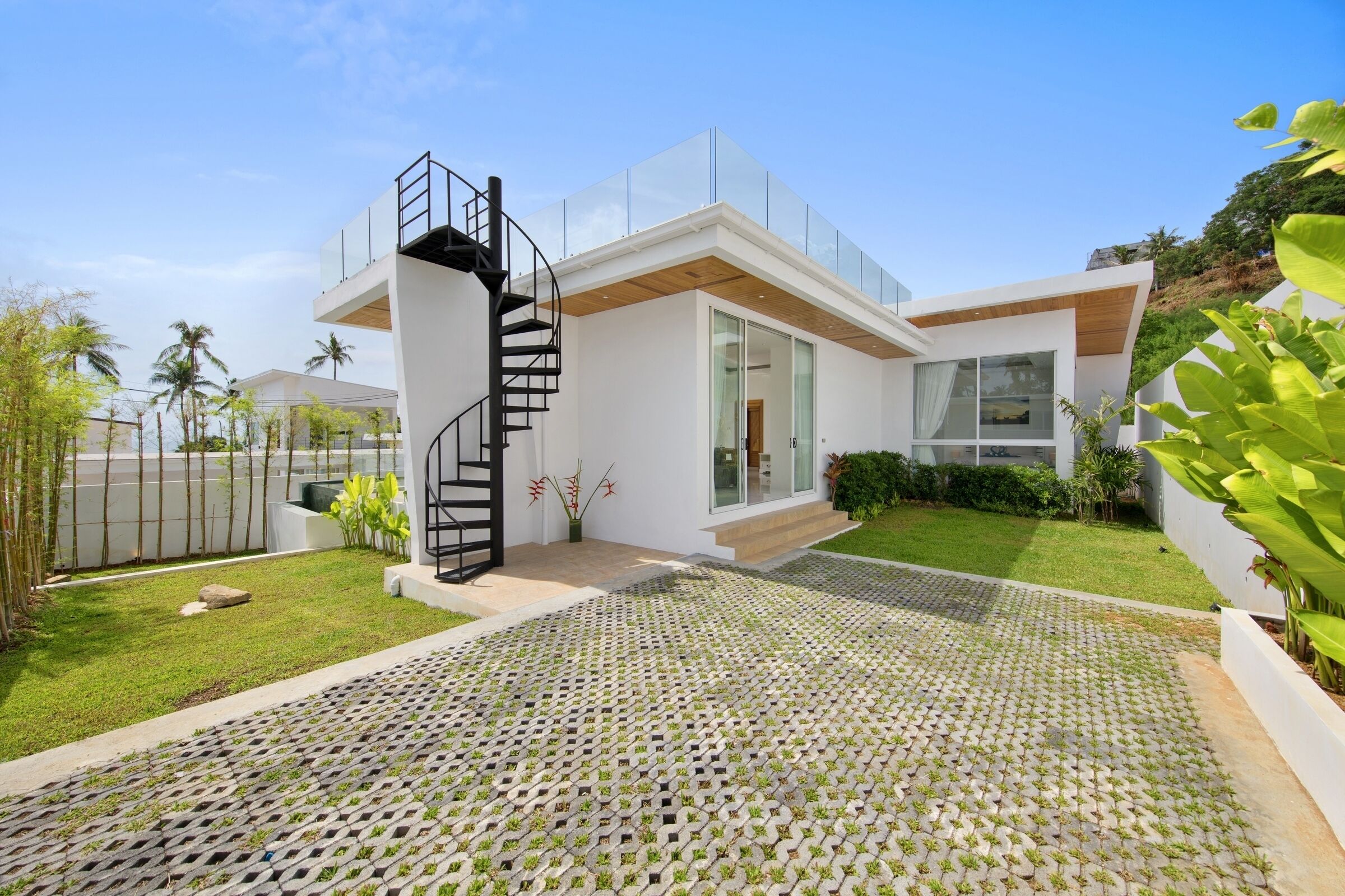 A modern house with a glass facade, a spiral staircase, and a well-maintained garden.