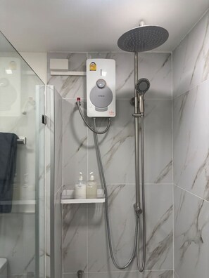 Ein modernes Badezimmer mit einer in Glas abgeschlossenen Dusche, einem Handbrausekopf und einer an der Wand montierten Bedienkonsole.