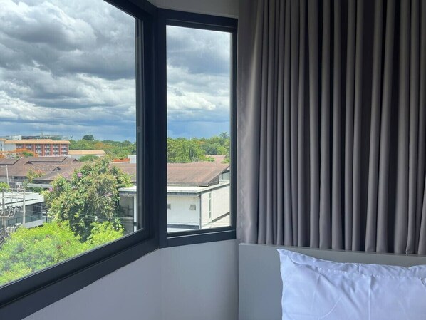 A hotel room with a large window, a bed, and a view of buildings and trees. - Warm and classic modern room (ตำ  บลสุเทพ)