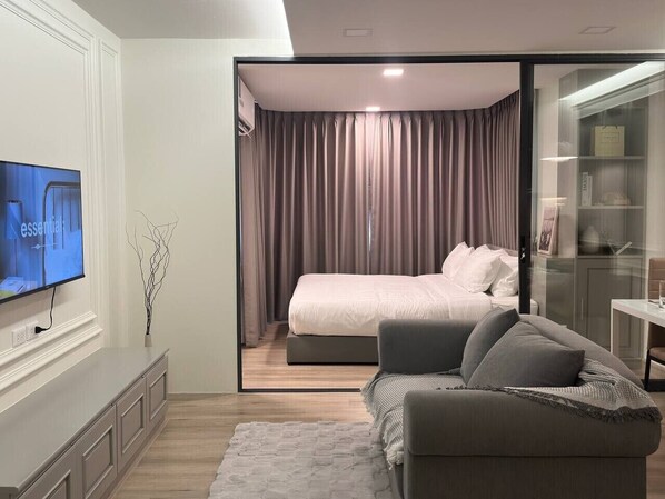 Un dormitorio moderno con cama, televisor y puerta de vidrio que da al baño.
