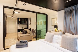 Habitación de hotel con cama, zona de estar con una silla, escritorio y kitchenette.
