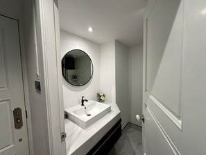 Un bagno con un lavandino bianco, uno specchio rotondo e un piccolo vaso con fiori.