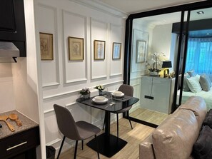 Un comedor moderno con una mesa de vidrio, dos sillas y una cocina visible a través de un separador de vidrio.