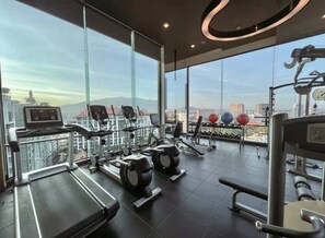 Une salle de sport équipée de tapis de course, de vélos elliptiques et d’appareils de musculation, avec une vue sur la ville grâce à de grandes fenêtres.