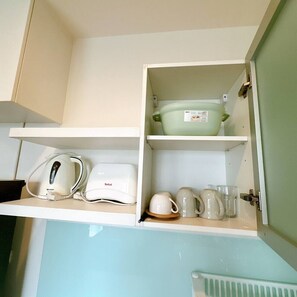 Una cocina con microondas, hervidor, tostadora, una olla verde y tazas y vasos en los estantes.