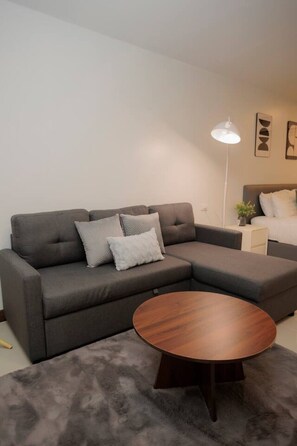 Ein modernes Wohnzimmer mit einem grauen Ecksofa, einem runden Couchtisch aus Holz und einer Stehlampe.