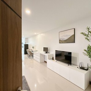 Ein modernes Wohnzimmer mit Flachbildfernseher, weißen Schränken und einem Essbereich im Hintergrund.