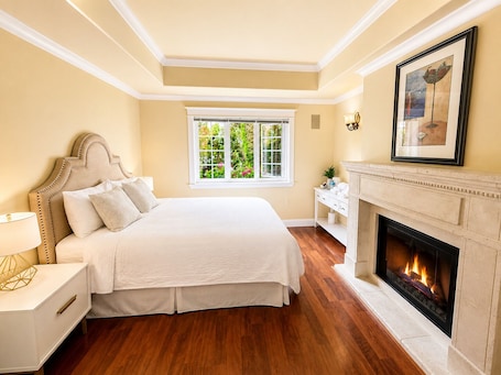 A bedroom with a bed, bedside table, nightstand, fireplace, and a window with a view of greenery.. Luxury 2 Bedrooms | 1,380 SF | Private Entrance | Free Parking