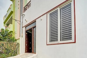 A residential building with a white facade, a window with horizontal blinds, and a door leading to the interior.