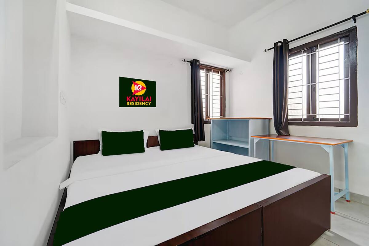 A bedroom with a bed, a desk, a window with curtains, and a sign on the wall.
