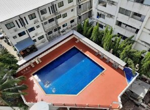 Una piscina sul tetto con un solarium rosso, circondata da edifici a più piani.
