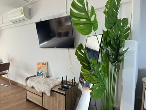 Una sala de estar moderna con un televisor de pantalla plana montado en la pared, una mesa de centro de madera con una manta de piel, una planta de Monstera grande y un jarrón blanco.