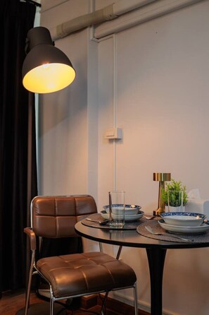 Un comedor con una mesa dispuesta para dos, una silla de cuero, una lámpara colgante y una pequeña planta en maceta.