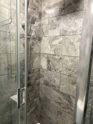 A glass-enclosed shower with a handheld showerhead and a wall-mounted control panel.