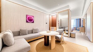 A modern hotel room with a sofa, a round table, a mirror, and a view of the city. - Crystal Hotel Qingdao Hi-Tech Convention (Qingdao)