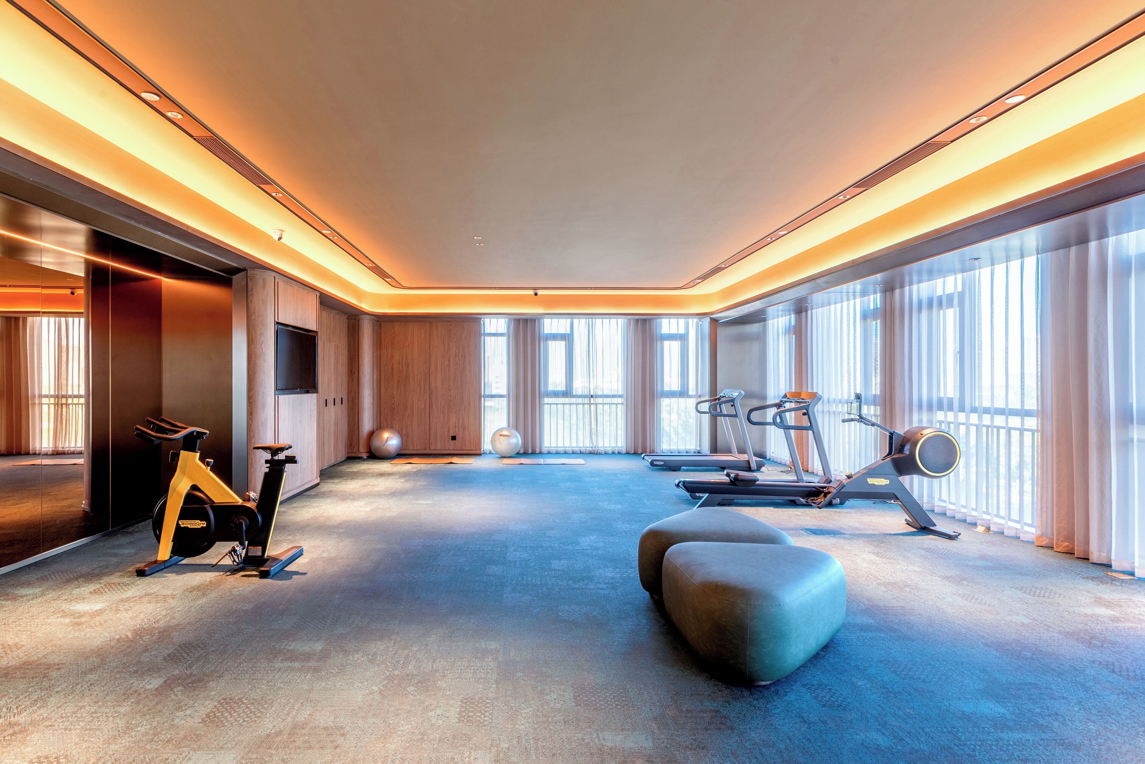 A spacious room with a large window, exercise equipment, and a soft seating area.