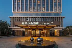 Moderni hotellin sisäänkäynti, jossa on kyltti, jossa lukee »Crystal Hotel», lasijulkisivu ja suihkulähde edessä.