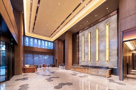 A spacious lobby with a reception desk, seating areas, and a large wall with vertical light fixtures.. Crystal Hotel Qingdao Hi-Tech Convention
