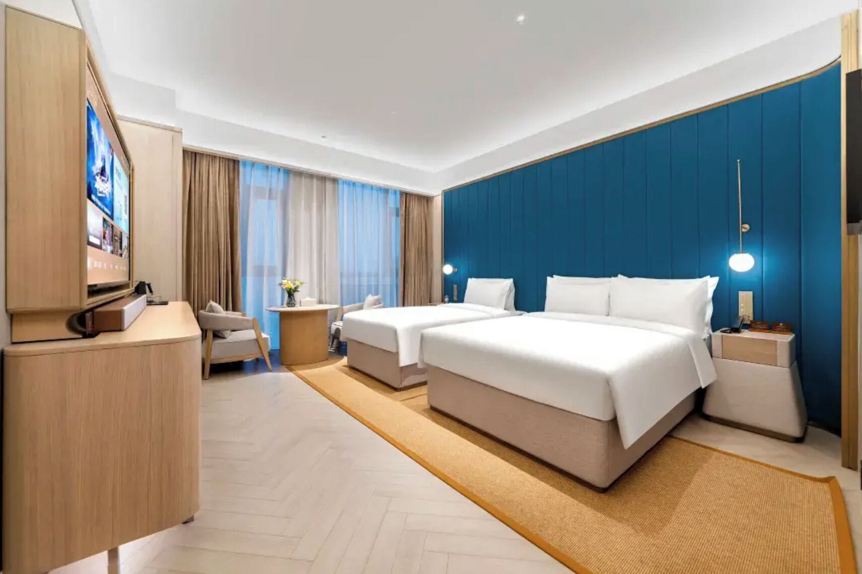 A hotel room with a large bed, a desk, a chair, a TV, and a blue accent wall.