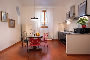 Une cuisine compacte avec un coin repas, comprenant une table ronde, des chaises, un luminaire suspendu et une fenêtre avec des rideaux.