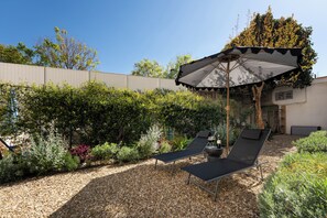 Een tuin met twee loungestoelen, een tafel en een grote parasol.