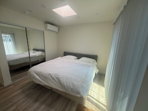 A bedroom with a bed, a mirror, an air conditioning unit, and a window with blinds.