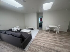 Een moderne woonkamer met een grijze bank, een witte salontafel en een eethoek met een witte tafel en stoelen.