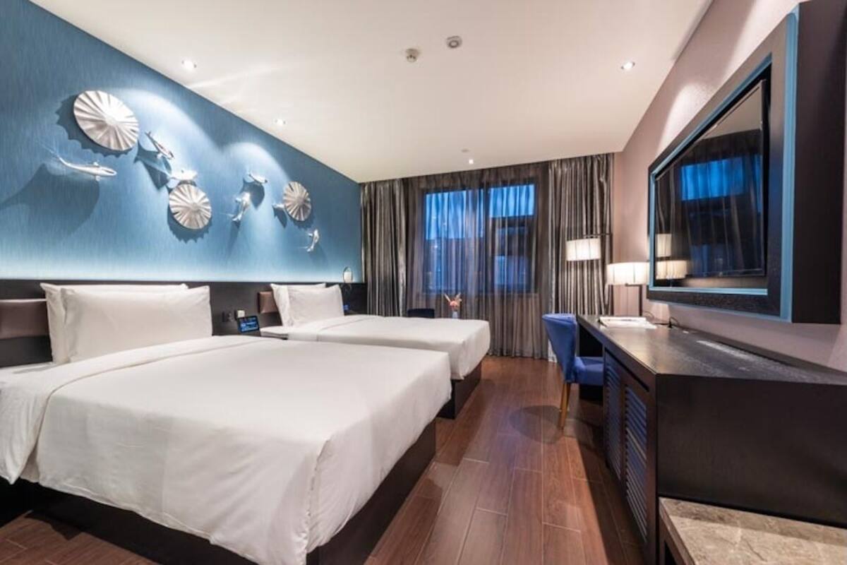 A hotel room with two beds, a desk, a mirror, and a wall with decorative plates.