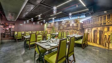 Un restaurante con sillas verdes, mesas dispuestas con platos y cubiertos, y un mural en la pared.