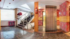 A hotel lobby with a marble floor, a staircase, a fire extinguisher, and a red wall with a decorative pattern. - Lords Inn Amritsar (Amritsar)