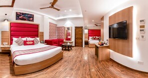 A modern hotel room with a curved bed, a TV, a desk, and a seating area with red chairs. - Lords Inn Amritsar (Amritsar)