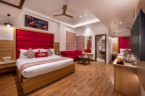 A modern hotel room with a large bed, a red upholstered headboard, a ceiling fan, and a small seating area. - Lords Inn Amritsar (Amritsar)
