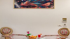 A room with a bed, two chairs, a small table with fruit and a drink, and a painting on the wall. - Lords Inn Amritsar (Amritsar)