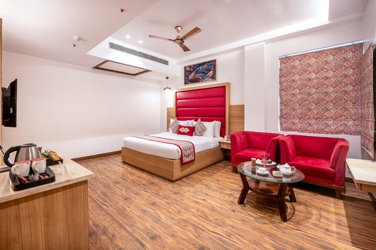 A hotel room with a bed, a red sofa, a small table with a teapot, and a coffee machine.