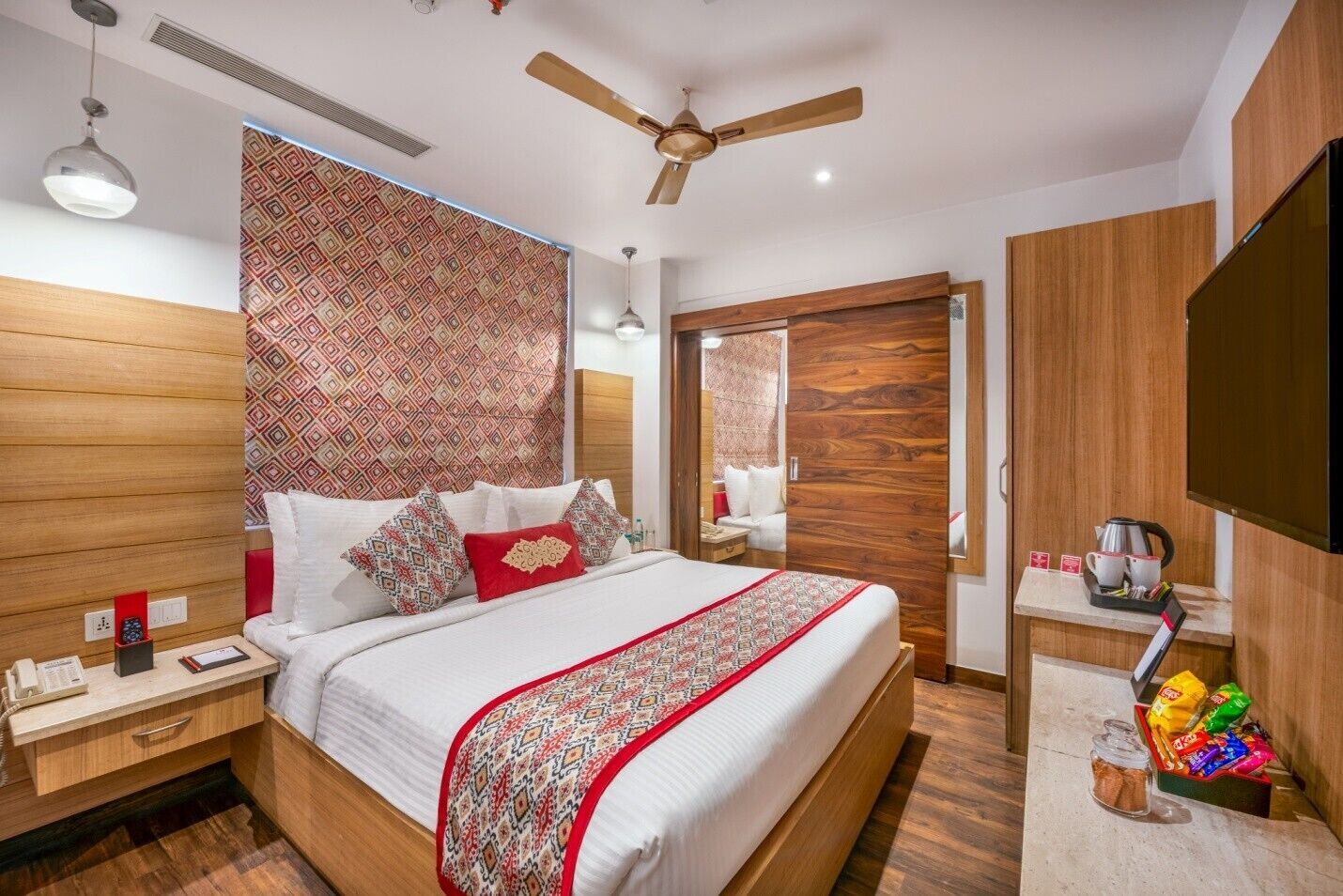Un dormitorio moderno con una cama grande, cabecera de madera, ventilador de techo y mesita de noche con lámpara.