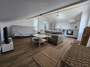 Ein kompakter Wohnbereich mit Sofa, kleinem Tisch, Fernseher und Küchenzeile.