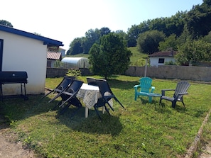 Un espacio al aire libre con césped, una parrilla, una mesa con sillas y un invernadero.