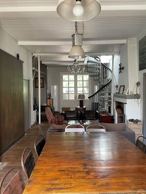 A spacious dining area with a long wooden table, a chandelier, and a spiral staircase.