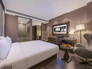 Habitación de hotel con una cama, televisor, escritorio con silla y una mesita con fruta.