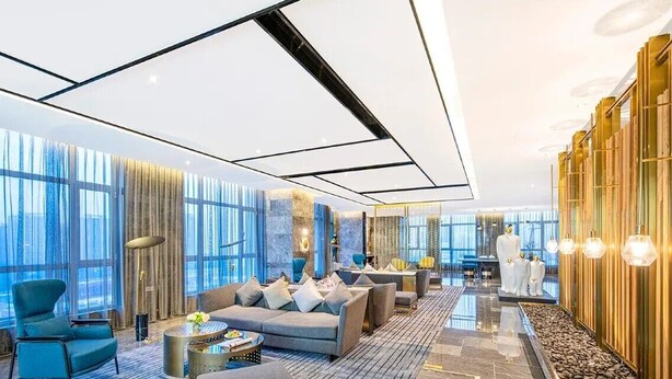 A modern hotel lobby with a sofa, chairs, a coffee table, and a decorative wall.