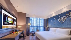 A hotel room with a bed, a desk with a TV, a small table with a vase, and a wall with butterfly decorations.