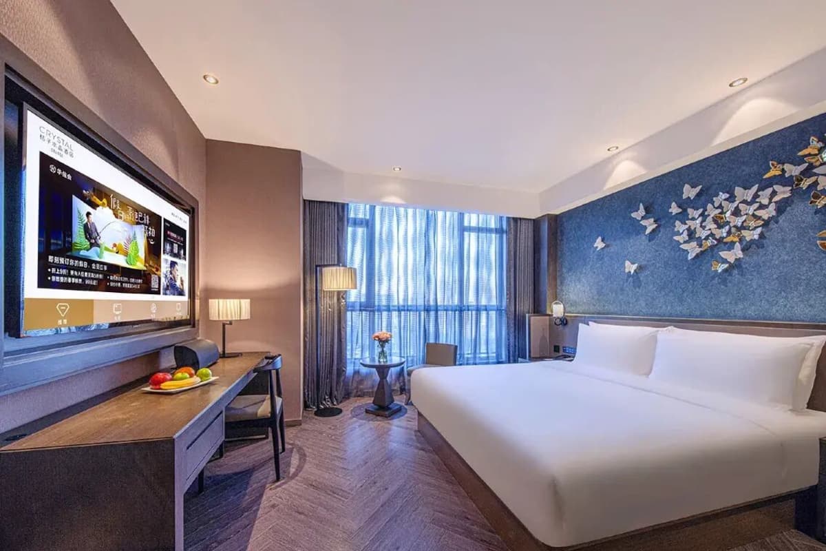 Habitación de hotel con cama, escritorio con televisor, mesita con un florero y pared decorada con mariposas.