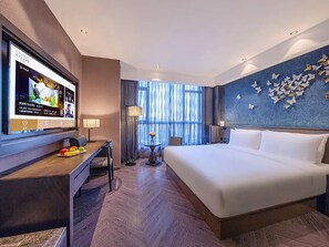 Une chambre d’hôtel avec un lit, un bureau avec une télévision, une petite table avec un vase et un mur décoré de motifs de papillons.
