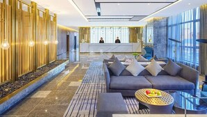 A modern lobby with a reception desk, seating area, and large windows.