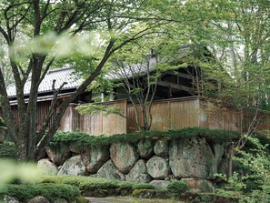 Un bâtiment traditionnel en bois, doté d’un toit en tuiles, entouré de gros rochers et d’une végétation luxuriante.