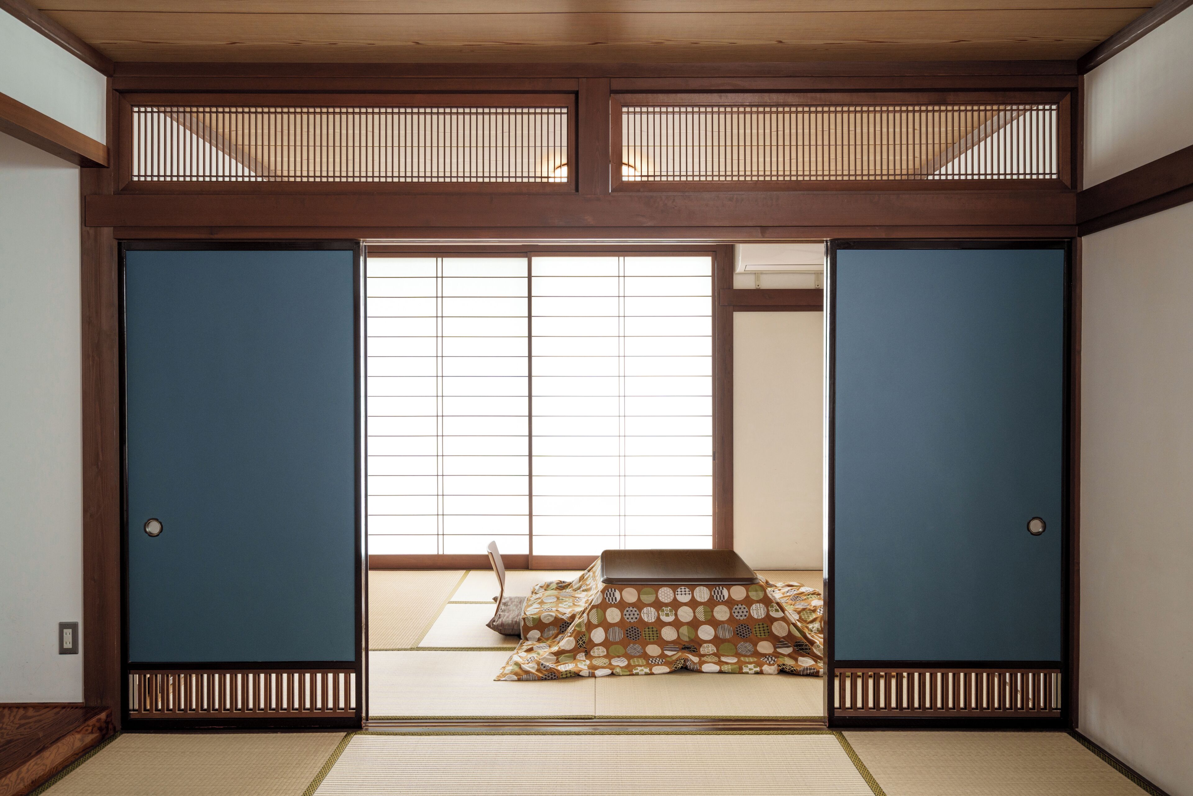 A traditional Japanese room with tatami flooring, shoji screens, and a low table with cushions.