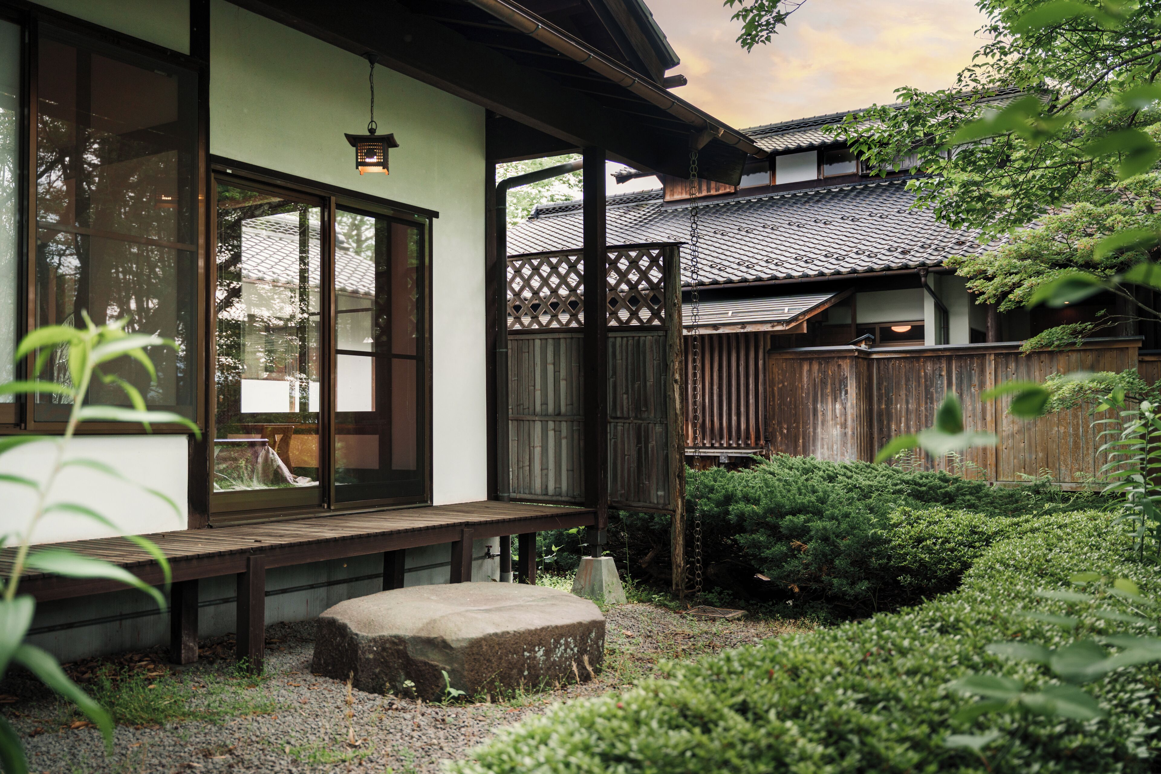 A traditional Japanese house with a wooden deck, a stone lantern, and a wooden fence.