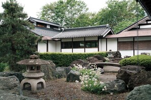 Un edificio japonés tradicional con tejado de tejas, rodeado por un jardín de rocas y una pequeña pagoda.
