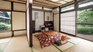 A traditional Japanese room with tatami flooring, a low table, and a view of greenery outside.